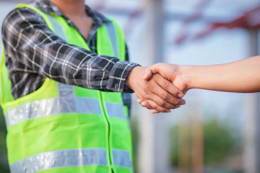 Torso view of a man in safety vest shaking hands with someone off camera.