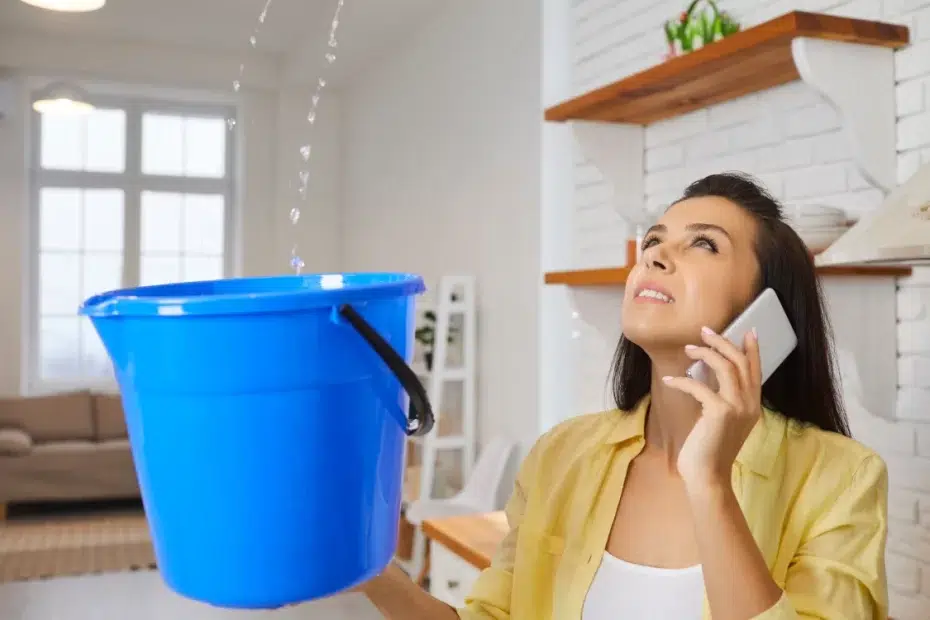 Woman on cell phone looking up catching leaking water in bucket